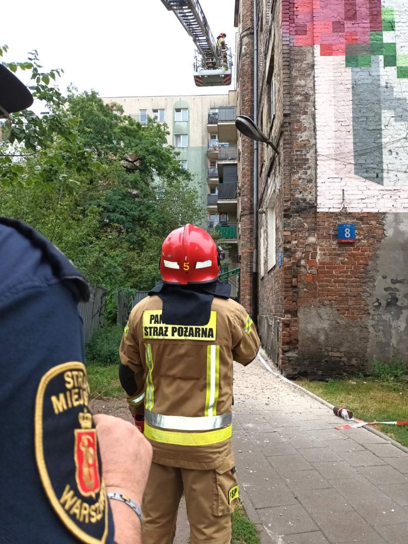 Strażnik miejski i strażak przed fasadą zniszczonego budynku z cegły.