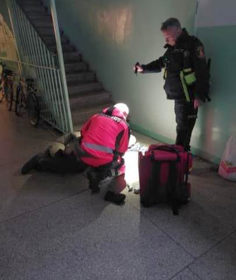 Strażnik miejski asystujący ratownikowi medycznemu podczas udzielania pomocy leżącemu na ziemi mężczyźnie