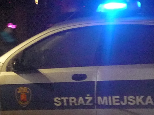 Zdjęcie ilustracyjne- radiowóz straży miejskiej nocą z włączonymi światłami sygnalizacyjnymi