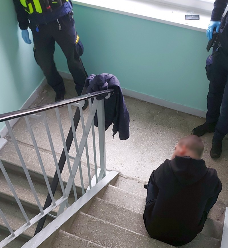 Strażnicy miejscy stoją obok siedzącego na schodach mężczyzny.
