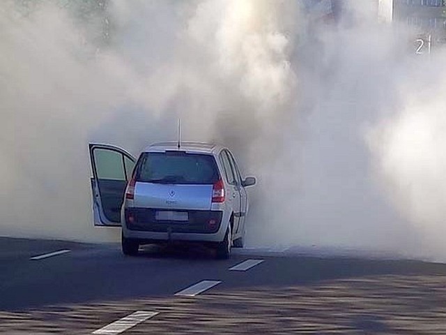 Zdjęcie z interwencji: widziany od tyłu stojący na jezdni biały ford, z otwartymi drzwiami od strony kierowcy. Wokół niego kłębiąca się chmura gęstego dymu.