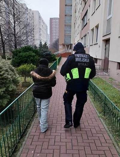 Zdjęcie z interwencji: kobieta idzie chodnikiem wzdłuż budynku, po jej prawej stronie idzie strażnik miejski.