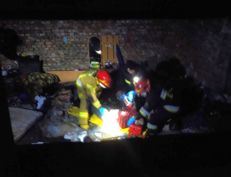 Zdjęcie z interwencji: strażnik i dwóch strażaków pochyla się na leżącym na ziemi mężczyzną. 