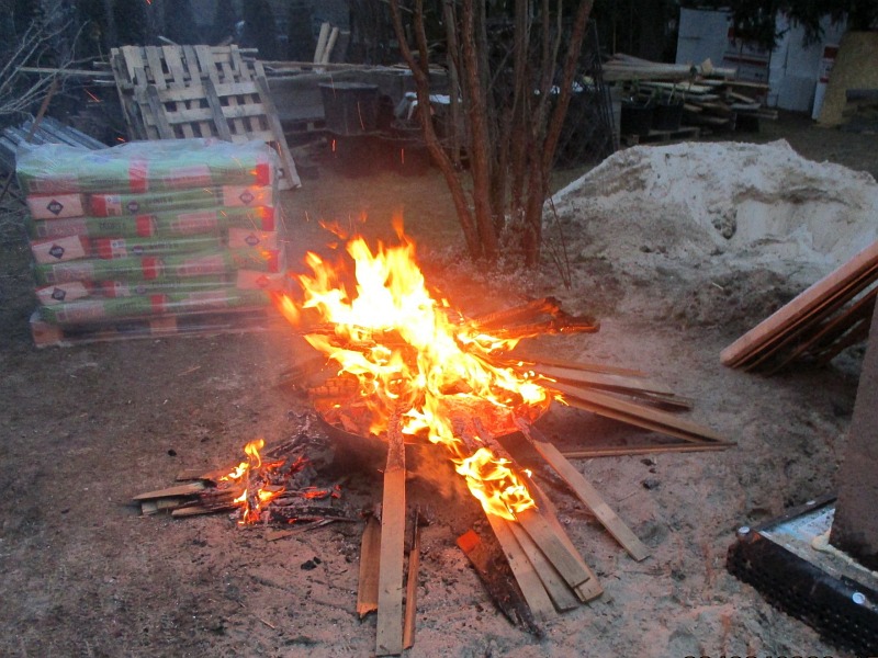 Zdjęcie z interwencji: ognisko, w którym spalane były odpady. W tle materiały budowlane i drewniana paleta.