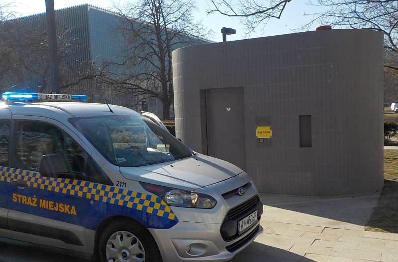 Zdjęcie z interwencji: radiowóz straży miejskiej stojący przy toalecie, w której zamknęło się trzech mężczyzn.