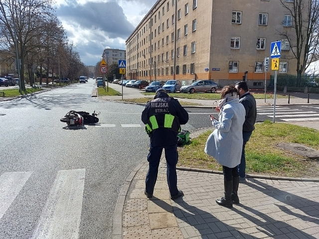 Zdjęcie z interwencji: na chodniku stoi strażnik miejski, obok niego kobieta i mężczyzna. Nieco dalej, na skrzyżowaniu, leży przewrócony skuter.