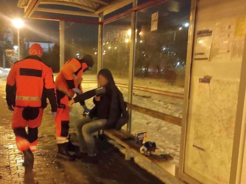 Narkoman na przystanku autobusowym. Obok niego ratownicy pogotowia ratunkowego.