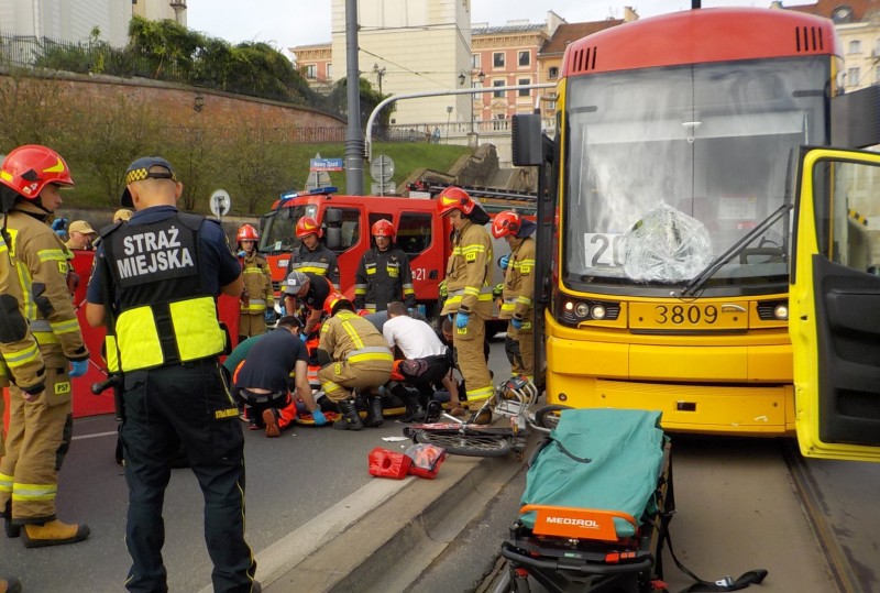 Akcja ratunkowa na przystanku: strażacy i strażnicy pomagają poszkodowanemu leżącemu obok stojącego na torowisku tramwaju