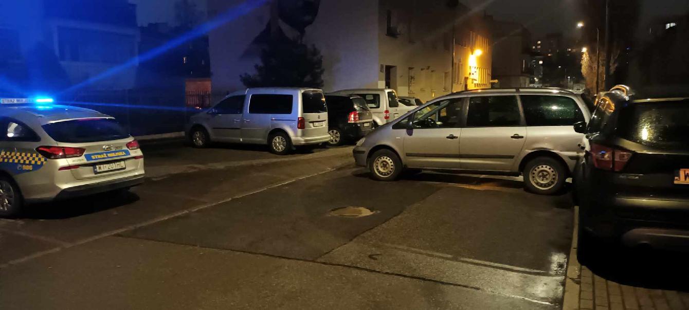 Kolizja samochodów. Jeden zaparkowany na skraju chodnika, drugi oparty o niego tyłem. Za boku radiowóz straży miejskiej.