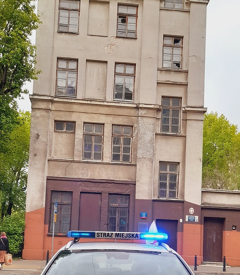 Radiowóz straży miejskiej prze zdewastowanym budynkiem