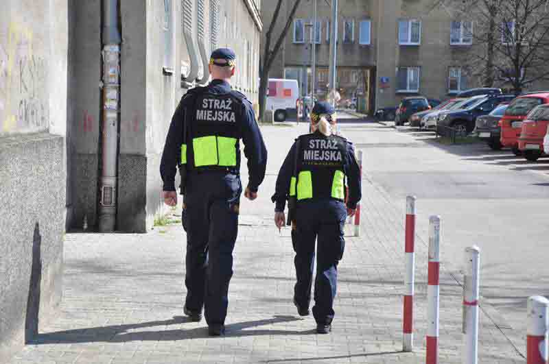 Patrol straży miejskiej idzie chodnikiem wzdłuż ulicy