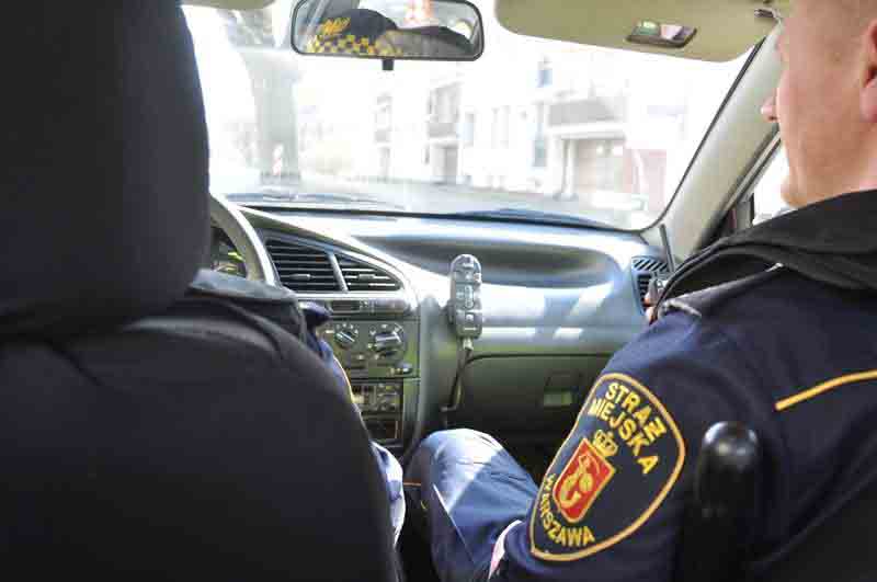 Zdjęcie ilustracyjne: strażnik miejski siedzący w radiowozie, na miejscu dla pasażera.