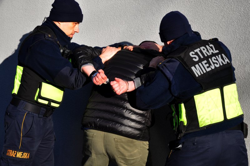 Strażnicy miejscy trzymający mężczyznę zakutego w kajdanki- zdjęcie ilustracyjne