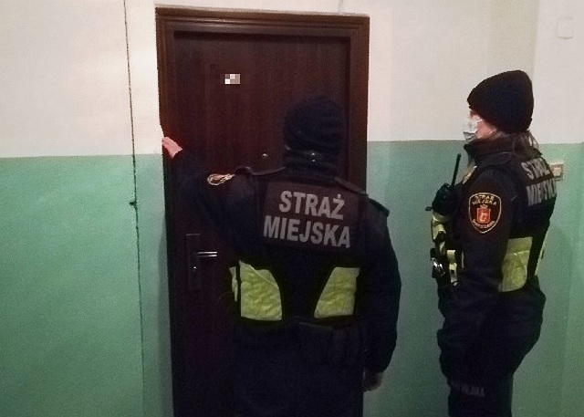 Zdjęcie ilustracyjne: patrol straży miejskiej przed drzwiami do mieszkania.