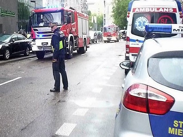 Zdjęcie ilustracyjne: strażnik miejski zabezpieczający miejsce pożaru. W tle samochód straży pożarnej oraz ambulans pogotowia.