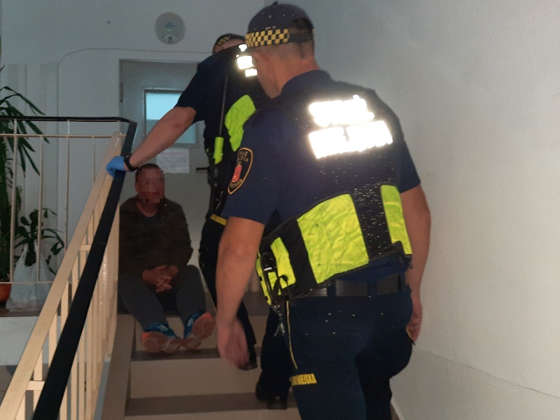 Zdjęcie ilustracyjne: dwóch strażników miejskich na klatce schodowej podchodzi do siedzącego na schodach mężczyzny.