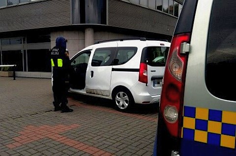 Zdjęcie ilustracyjne: strażnik miejski przy otwartych drzwiach samochodu osobowego. Na pierwszym planie fragment radiowozu straży miejskiej. 