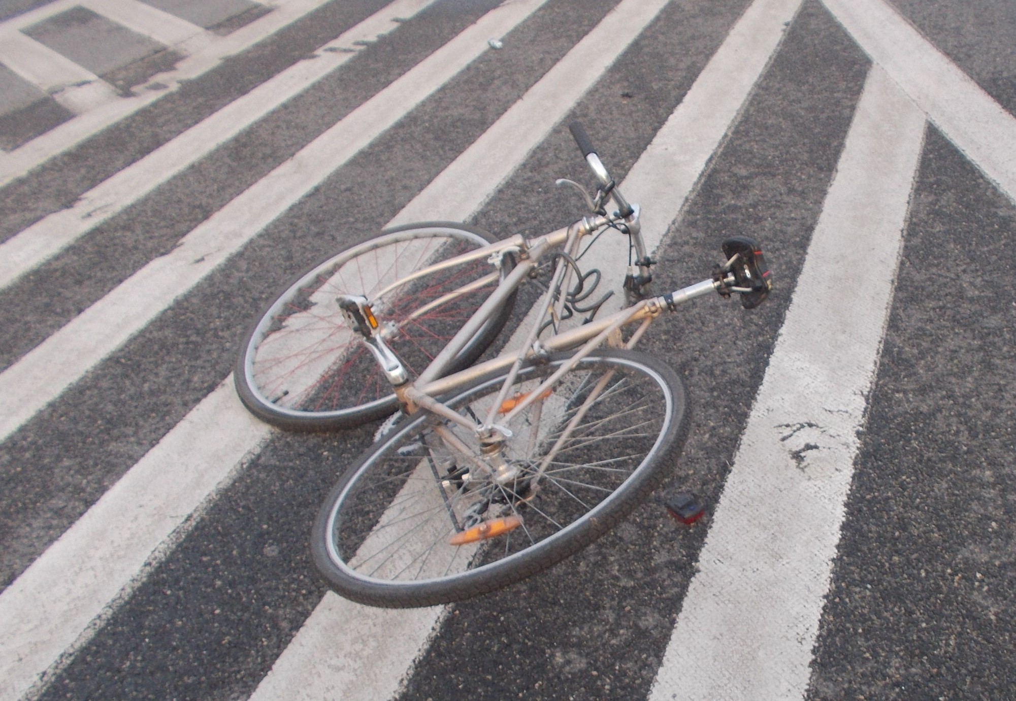 Lekko uszkodzony rower typu kolarzówka leży na jezdni (na powierzchni wyłączonej z ruchu).