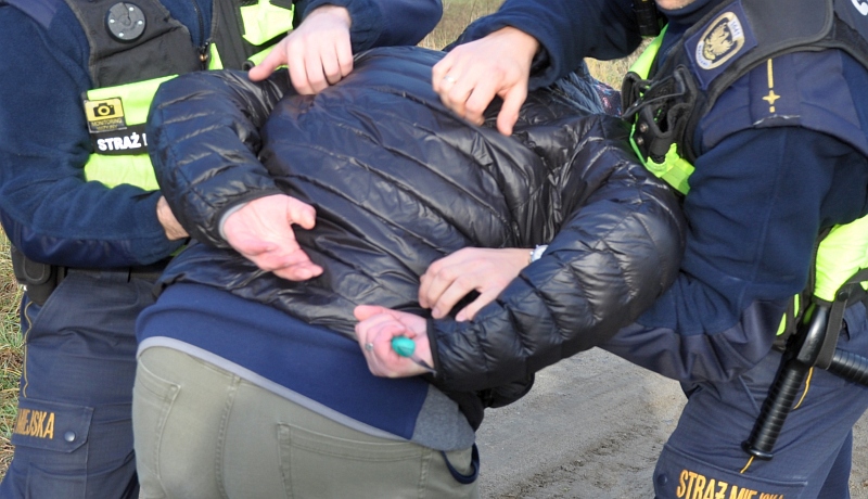Zdjęcie ilustracyjne: strażnicy miejscy przytrzymują wykręcone do tyłu ręce mężczyzny trzymającego nóż.