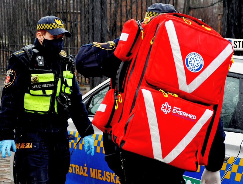 Zdjęcie ilustracyjne: strażnik- ratownik z plecakiem medycznym. Obok strażnik w pełnym umundurowaniu.