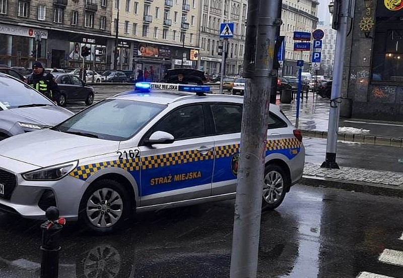 Zdjęcie ilustracyjne: radiowóz Straży Miejskiej podczas interwencji w Śródmieściu. Za nim, po lewej stronie, strażnik miejski podchodzący do samochodu mieszkańca.