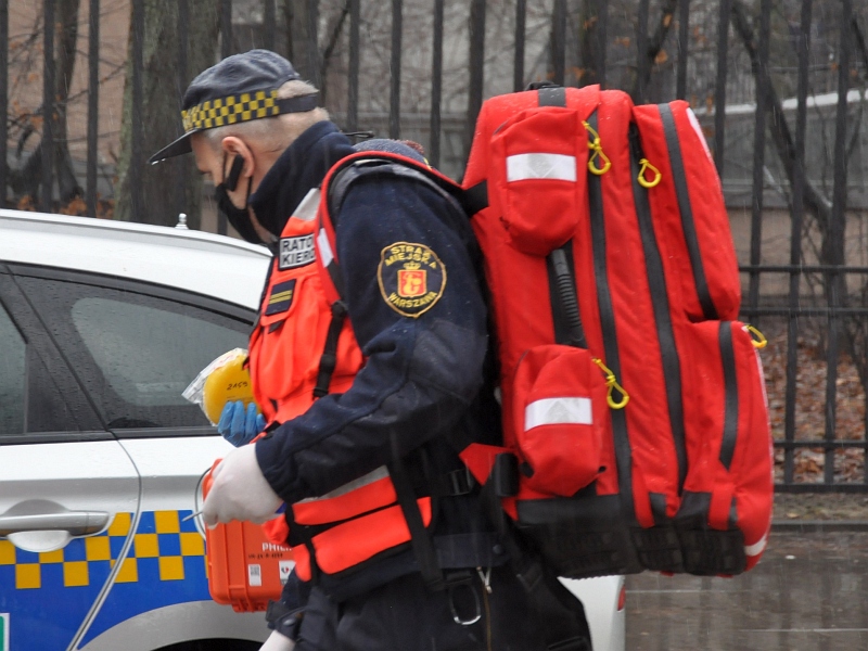 Zdjęcie ilustracyjne: strażnik miejski w kamizelce ratownika medycznego, z plecakiem ratunkowym na ramieniu.