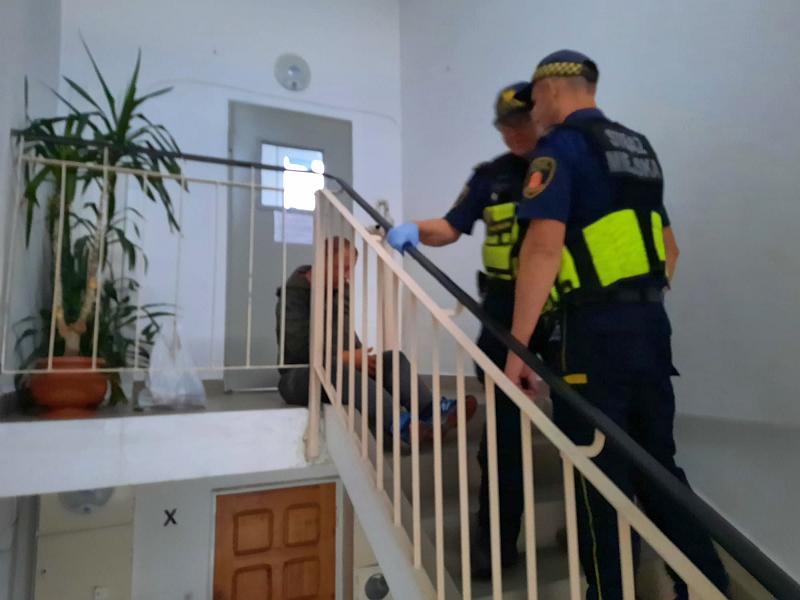 Zdjęcie ilustracyjne: strażnicy miejscy na klatce schodowej stoją obok mężczyzny siedzącego na schodach.
