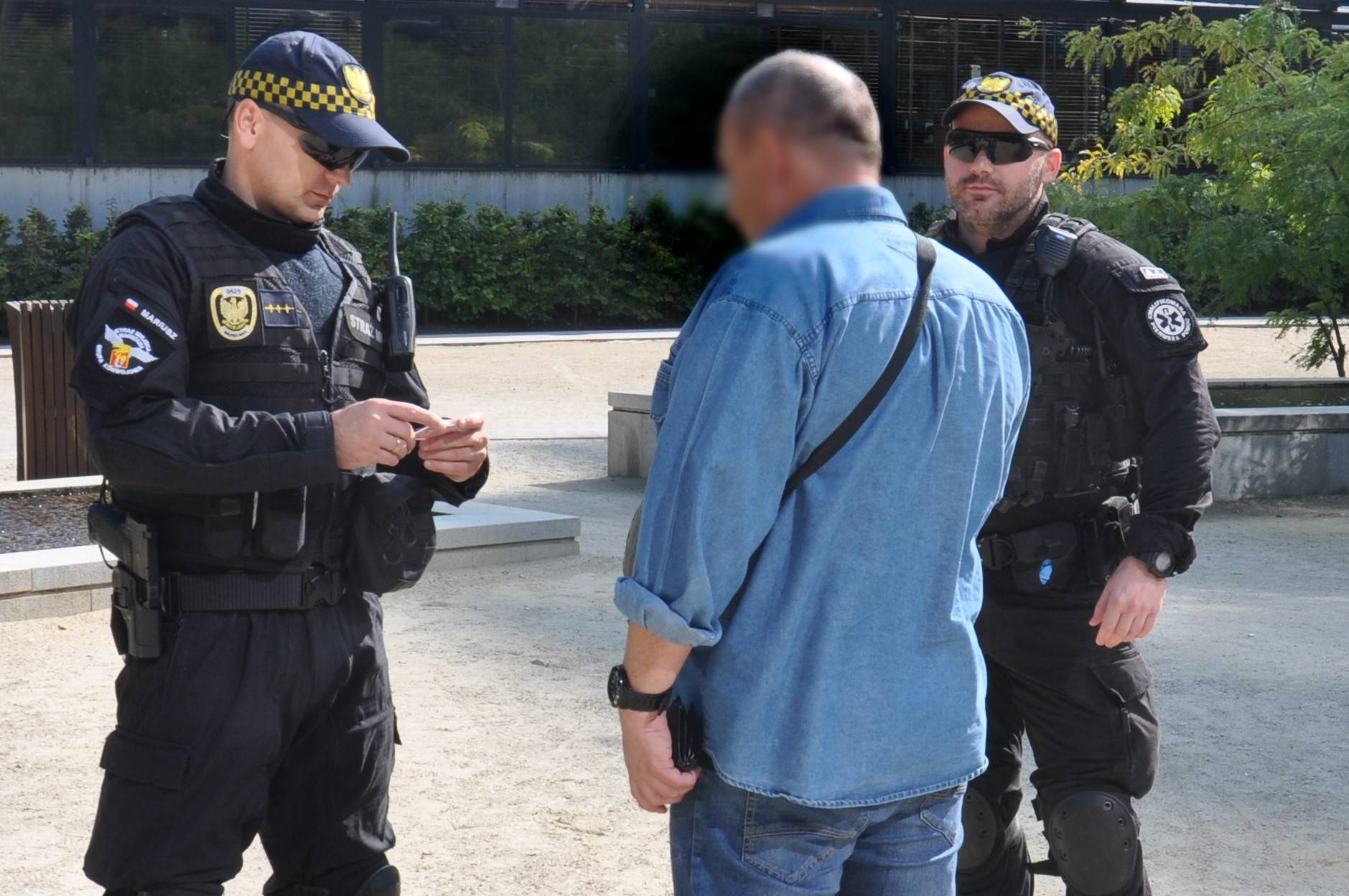 Strażnicy miejscy z oddziału specjalistycznego legitymują mężczyznę w dżinsowej koszuli.