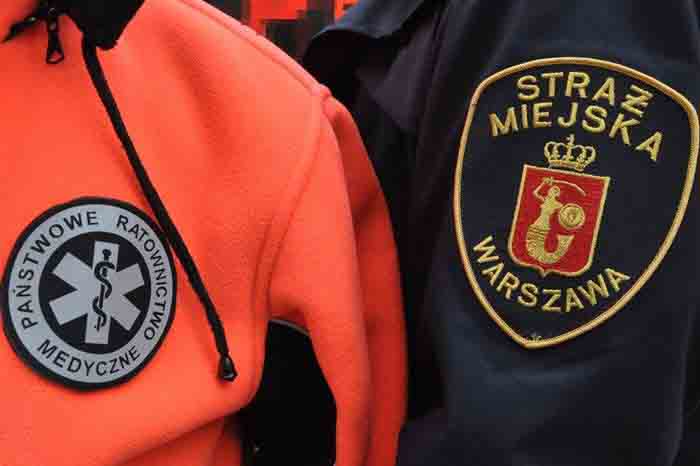 Zdjęcie ilustracyjne: fragment munduru z emblematem Straży Miejskiej obok kurtki ratownika medycznego Pogotowia Ratunkowego.