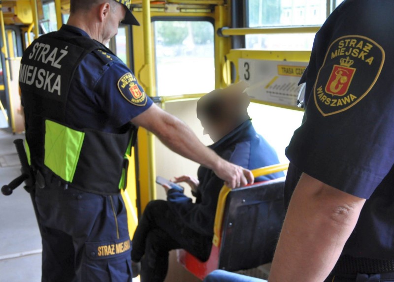 Strażnicy stojący obok siedzącej w tramwaju kobiety- zdjęcie ilustracyjne