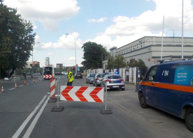 Strażnik miejski wygradza zapadlisko na Karowej. Obok, na poboczu, stoi samochód Wodociągów Warszawskich i radiowóz straży miejskiej.