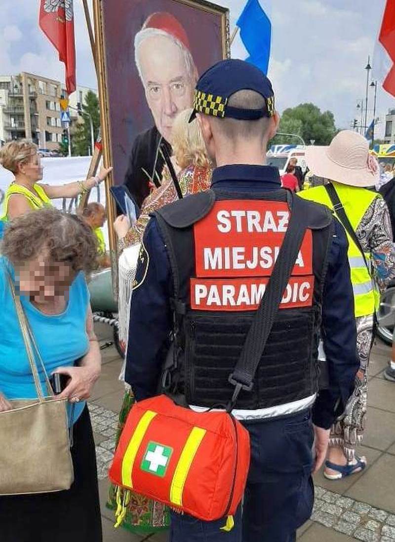 Uroczystości beatyfikacji kard. Wyszyńskiego- strażnik miejski z kamizelką "Paramedic" i apteczką przewieszoną przez ramię stojący przed portretem Prymasa.