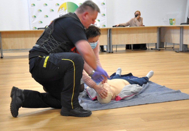 Zdjęcie ze spotkania: na podłodze leży fantom ćwiczebny, obok niego klęczy prowadzący szkolenie strażnik miejski instruując uczestniczkę, jak przeprowadzić masaż serca.