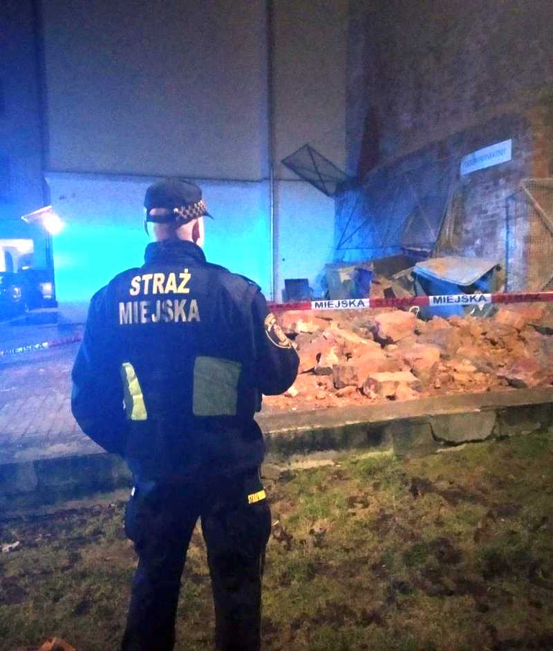 Zdjęcie z interwencji: strażnik miejski zabezpieczający miejsce zdarzenia- w tle stos cegieł z przewróconego muru.