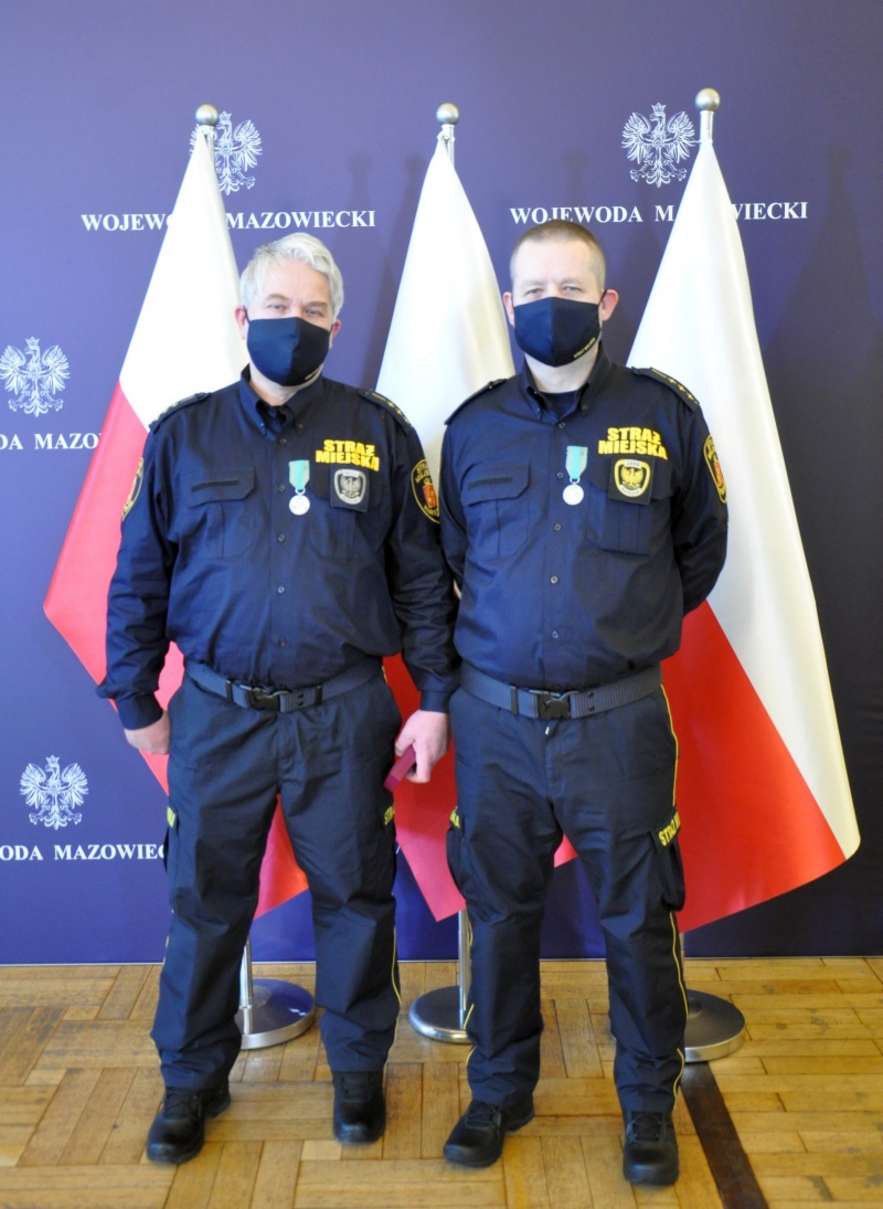 Inspektor Paweł Chilimończyk i inspektor Dariusz Herman z odznaczeniami, stoją na tle polskich flag.