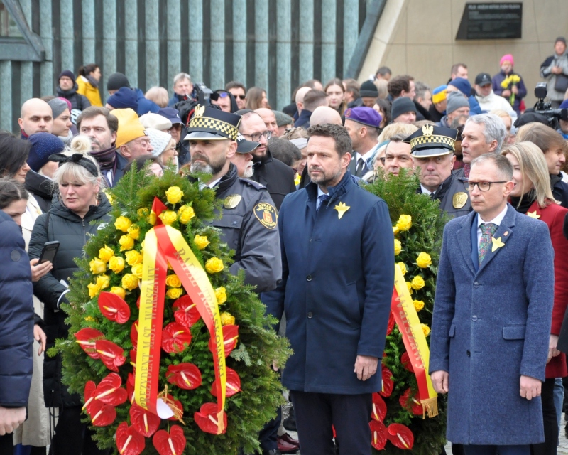 Zdjęcie z uroczystości: prezydent Warszawy wraz z delegacją urzędników składają wieniec pod pomnikiem Bohaterów Getta. Kwiaty niesie strażnik miejski.
