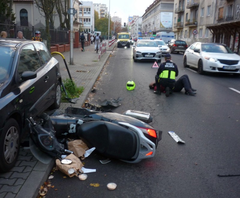 Wypadek na Chełmskiej: na jezdni leży przewrócony skuter, dalej , nad leżącym na asfalcie mężczyzną, klęczy strażnik miejski.