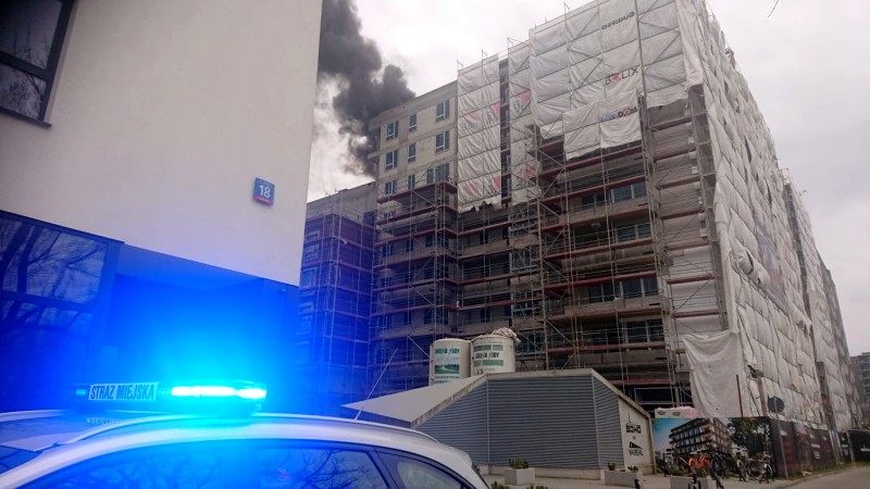Radiowóz straży miejskiej przed budynkiem, w którym trwa pożar