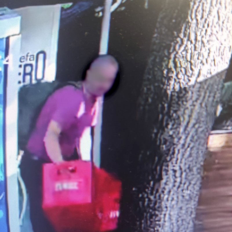 Zdjęcie z monitoringu- mężczyzna w różowej koszulce wynosi z lokalu skrzynkę z butelkami.