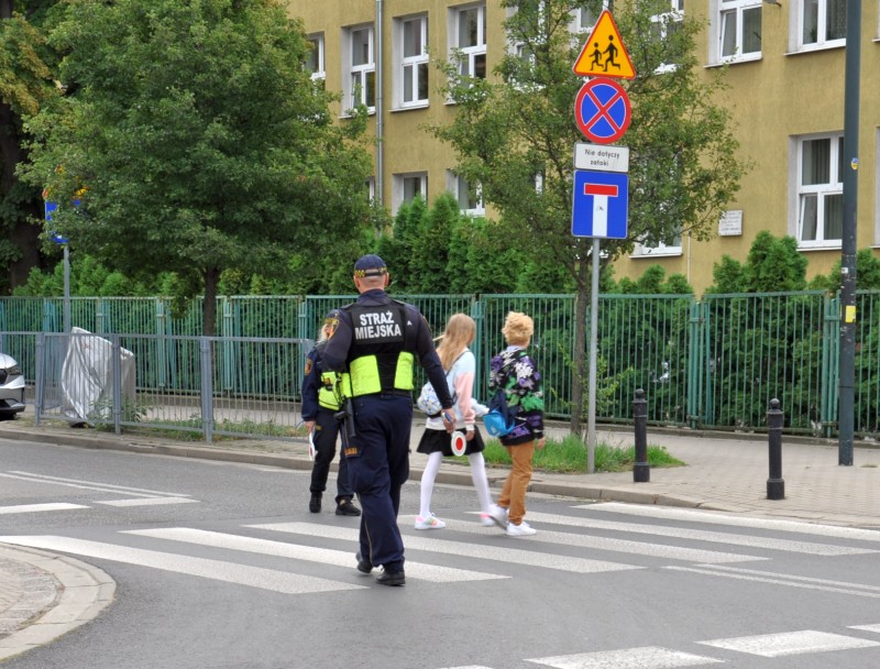 Strażnicy miejscy pomagają uczniom przejść przez jezdnię w pobliżu szkoły.