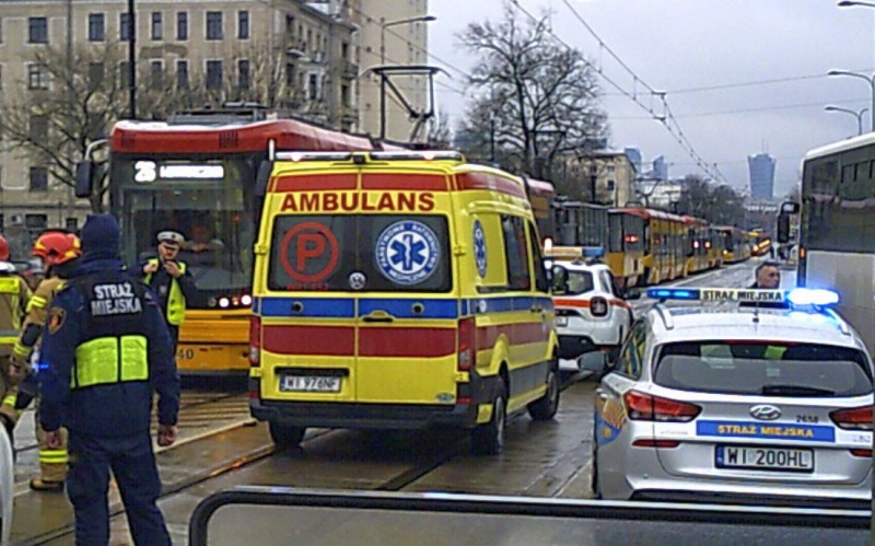Samochody służb ratunkowych na miejscu zdarzenia. Na pierwszym planie strażnik miejski obok radiowozu.