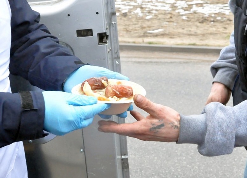 Strażnik miejski podający talerz z zupą bezdomnemu